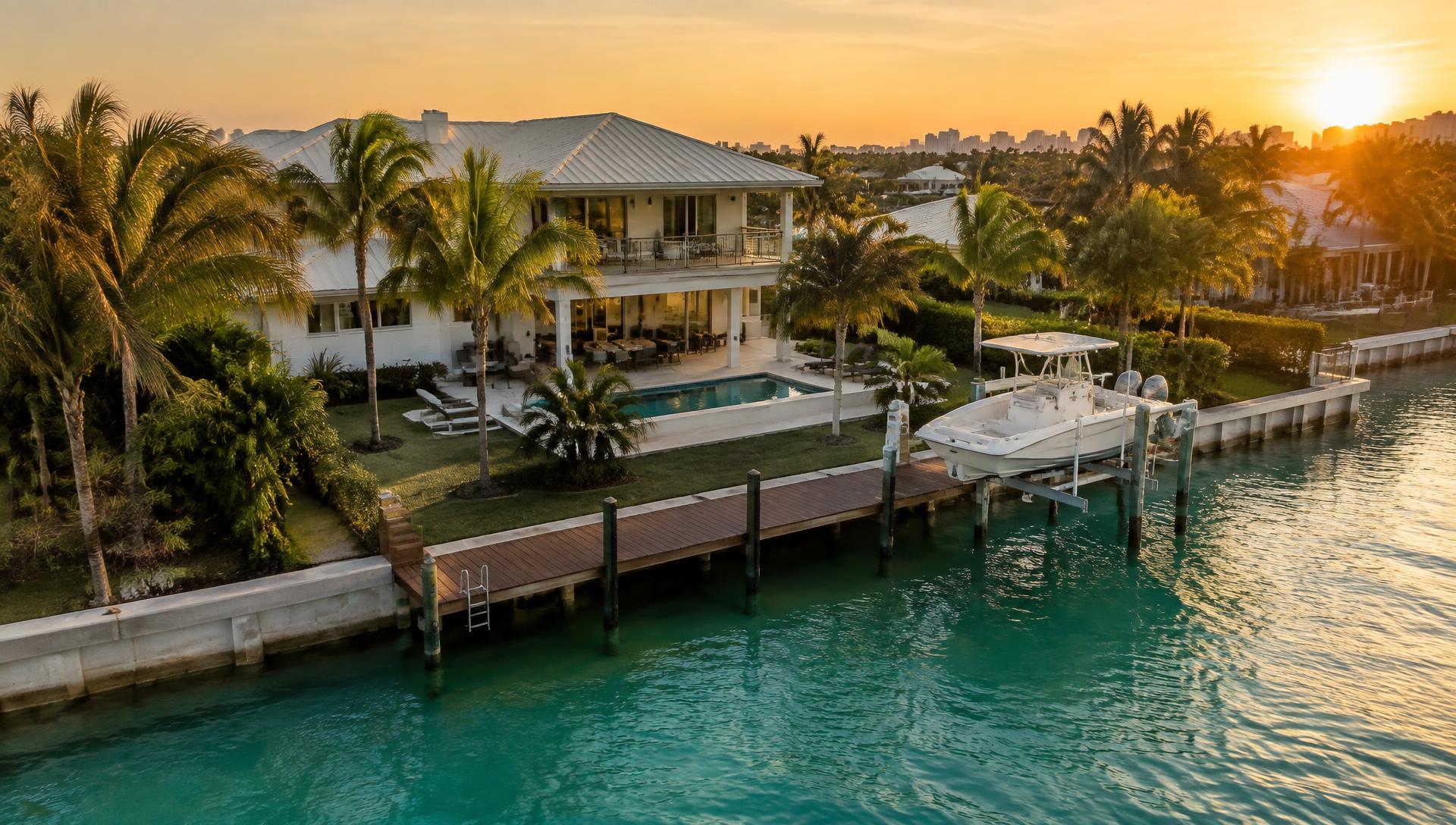 South Florida waterfront home with a concrete seawall, wood dock and boat on a lift at sunset